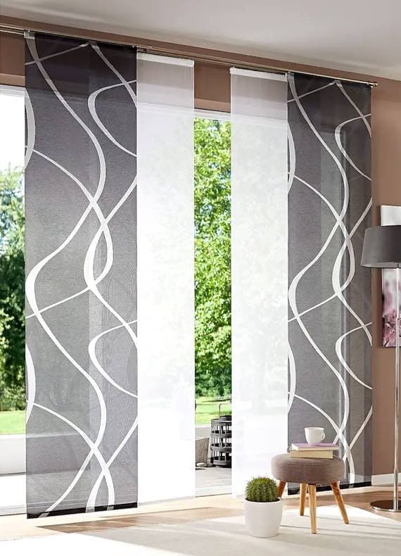 Schiebetür mit modernen Vorhängen in Grau-Weiß, dahinter grüner Garten, gemütliche Sitzecke mit Kaffeetasse und Buch