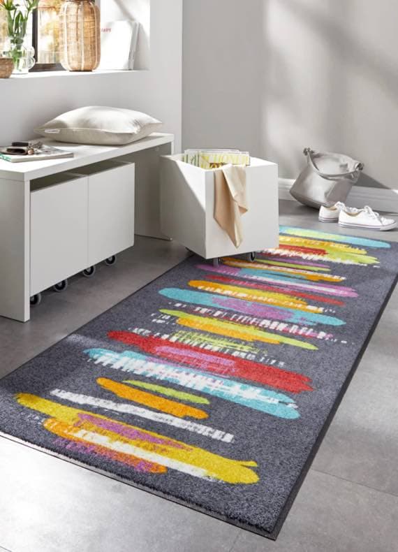 Bunter Teppich mit abstrakten Streifenmustern auf grauem Boden in modern eingerichteten Raum mit Bank und Dekoration.