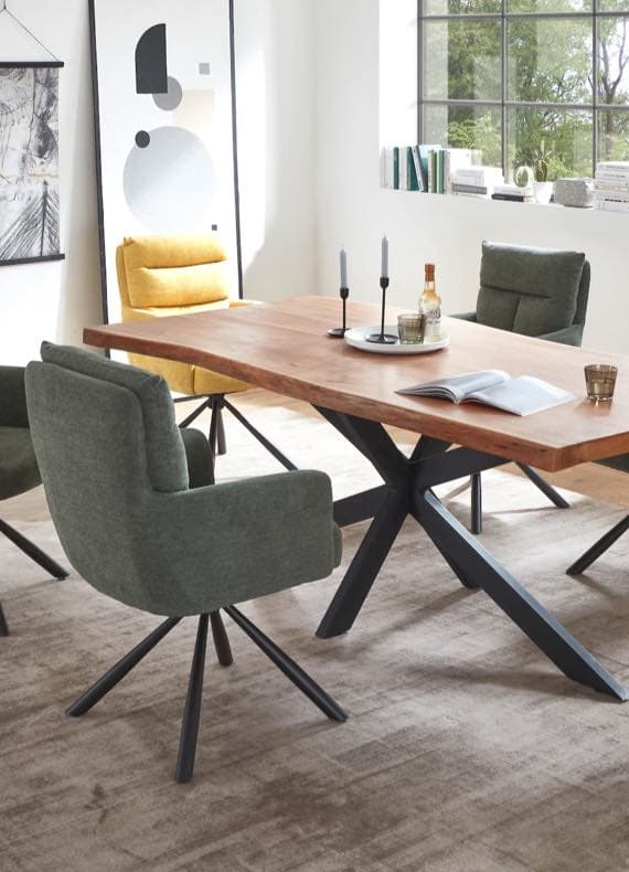 Essbereich mit Holztisch, grauen und gelben Stühlen, Kerzen, Buch und Flasche, Fenster im Hintergrund.