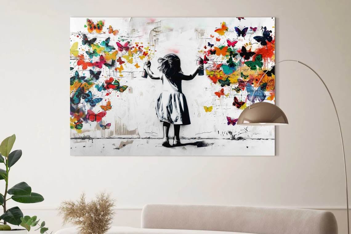 Ein Mädchen sprüht bunte Schmetterlinge an eine Wand, Kunstbild hängt an einer modernen Wohnzimmerwand.