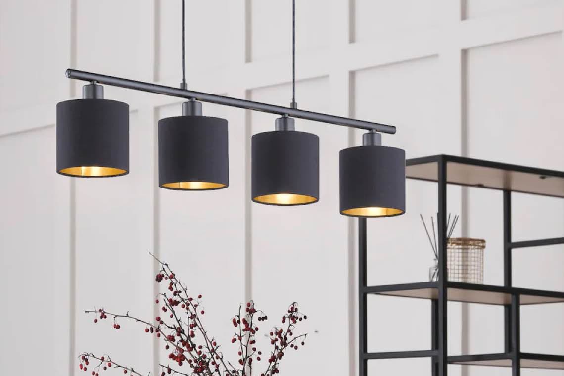 Schwarze Pendelleuchte mit vier Lampen über dekorativen Zweigen in modernem Raum mit Regal im Hintergrund.