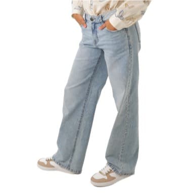 Person in hellblauen Jeans und Sneakers steht mit Händen in den Taschen.