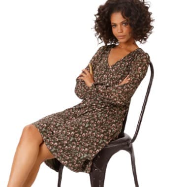 Frau in geblümtem Kleid sitzt mit verschränkten Armen auf Stuhl.