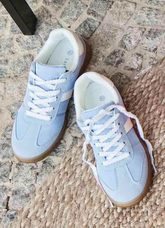 Hellblaue Sneaker mit weißen Schnürsenkeln auf Steinboden und Teppich.