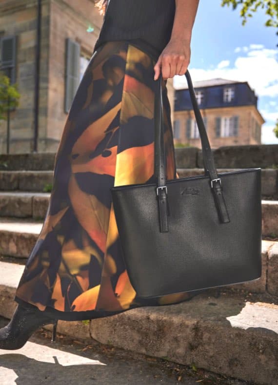 Person mit schwarzer Tasche und farbigem Rock steht auf Steintreppen im Freien.