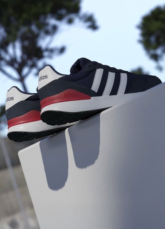 Zwei Adidas-Sneaker mit weißen Streifen und rotem Detail auf weißem Podest vor verschwommenen Bäumen.