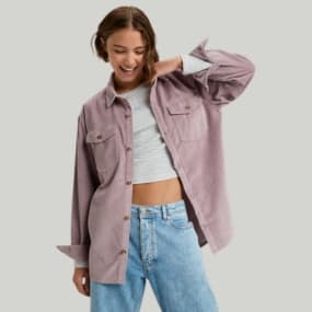 Frau trägt ein lila Cordhemd über einem gestreiften Crop-Top und blauen Jeans