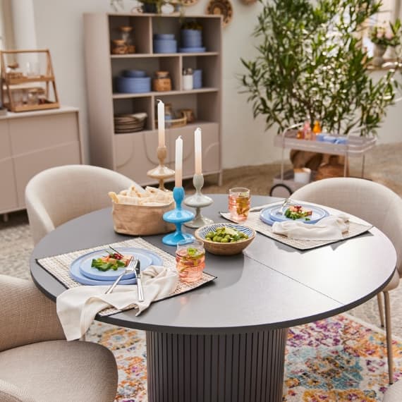 Gemütlich gedeckter Esstisch mit zwei Gedecken, Kerzenständern und Speisen, im Hintergrund ein Regal mit Geschirr.