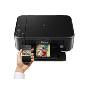 Schwarzer Canon-Drucker druckt Farbfoto – Hand hält Smartphone mit dem Foto darauf