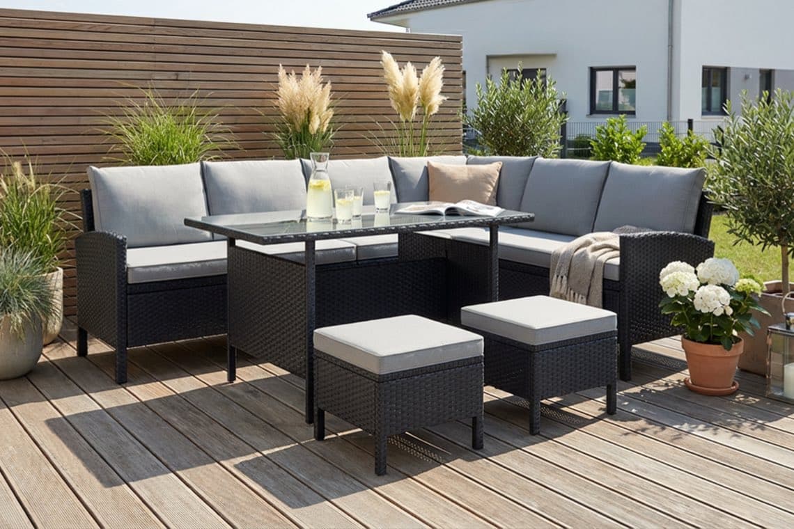 Eckige Gartenlounge mit grauen Polstern, Tisch mit Karaffe Zitronenwasser und Gläsern auf Holzterrasse, umgeben von Kübelpflanzen