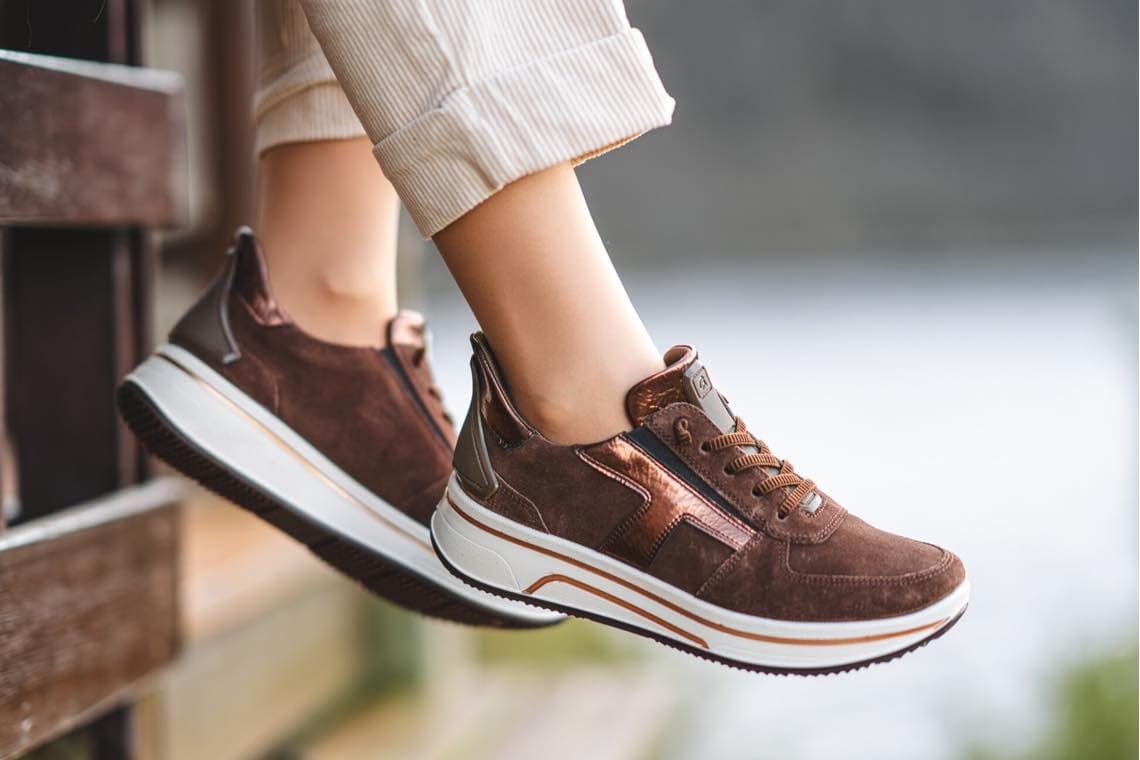 Beine in hellen Hosen mit braunen Sneakern vor verschwommenem Hintergrund