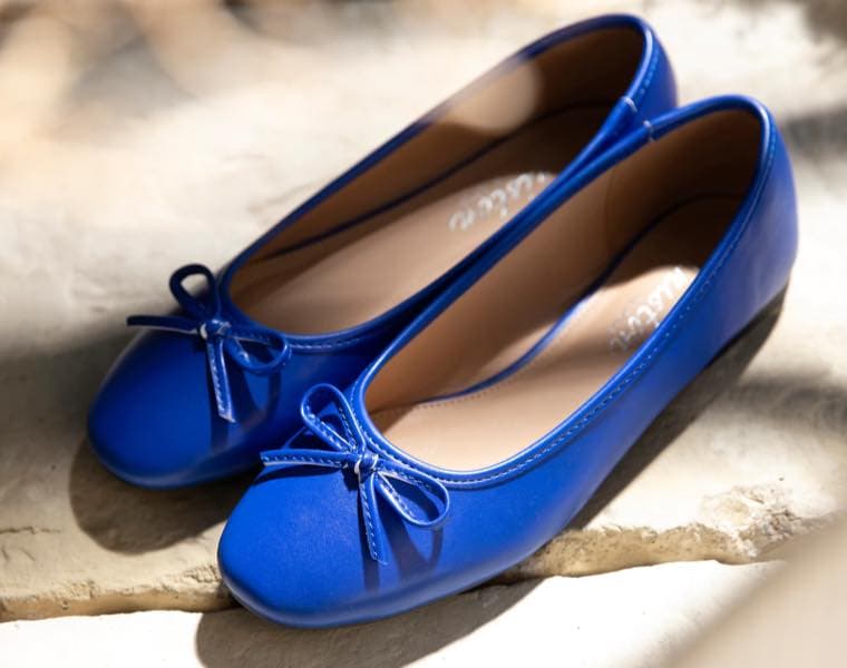 Zwei blaue Ballerinas mit Schleifen auf hellem Untergrund im Sonnenlicht