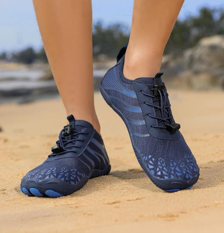 Person trägt dunkelblaue Barfußsschuhe am Strand.