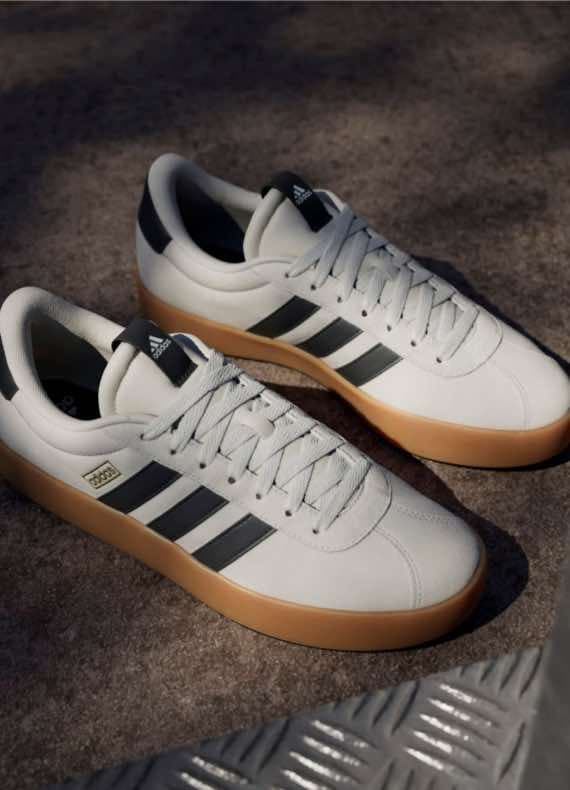 Zwei weiße Sneakers mit schwarzen Streifen und brauner Sohle auf grauem Hintergrund.