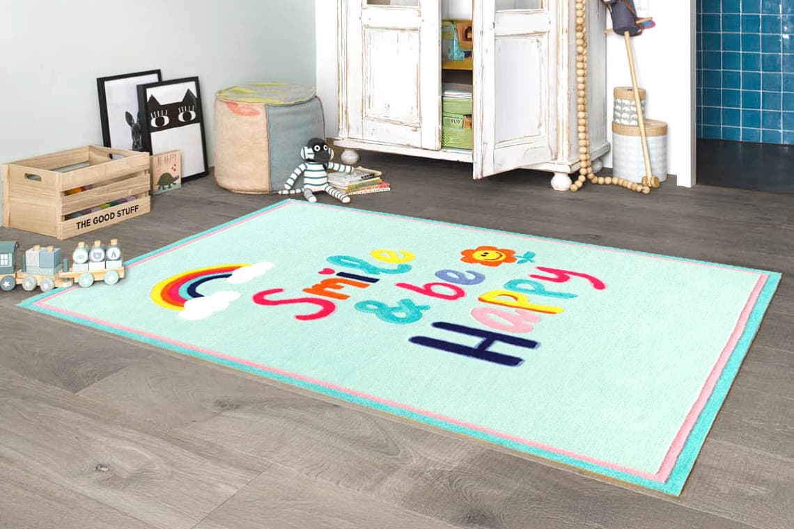 Smile & be Happy – bunter Kinderteppich mit Regenbogen und Blume in gemütlichem Spielzimmer mit Spielzeug und Sitzhocker