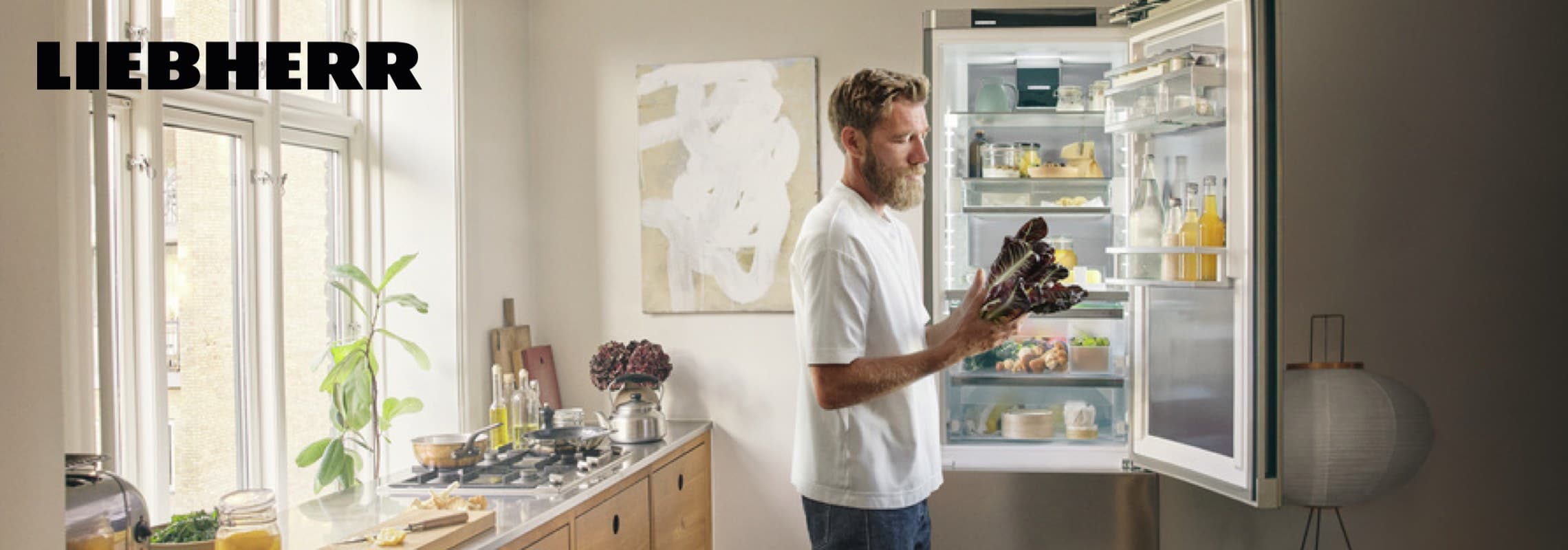 Liebherr – Person in heller Küche steht vor offenem Kühlschrank und hält frischen Salat in den Händen