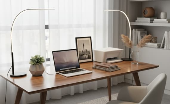 Modern Büro mit Laptop, Drucker, Pflanzen und zwei schlanken Lampen auf Holzschreibtisch vor Fenster.