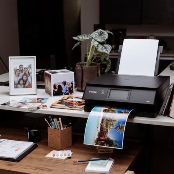 Canon-Drucker auf Tisch, druckt Foto von Strand, umgeben von weiteren Fotos, Pflanzen und Schreibwaren.