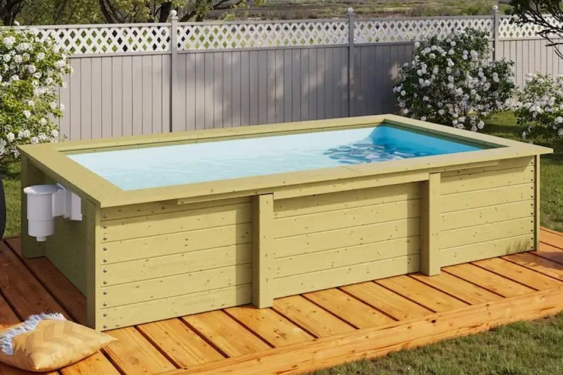 Rechteckiger Aufstellpool auf Holzterrasse im Garten vor Zaun und blühenden Sträuchern