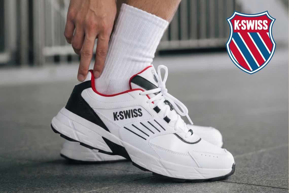 K-SWISS – Person zieht weißen Sneaker mit schwarzen Details an, daneben das K-SWISS Logo auf grauem Boden