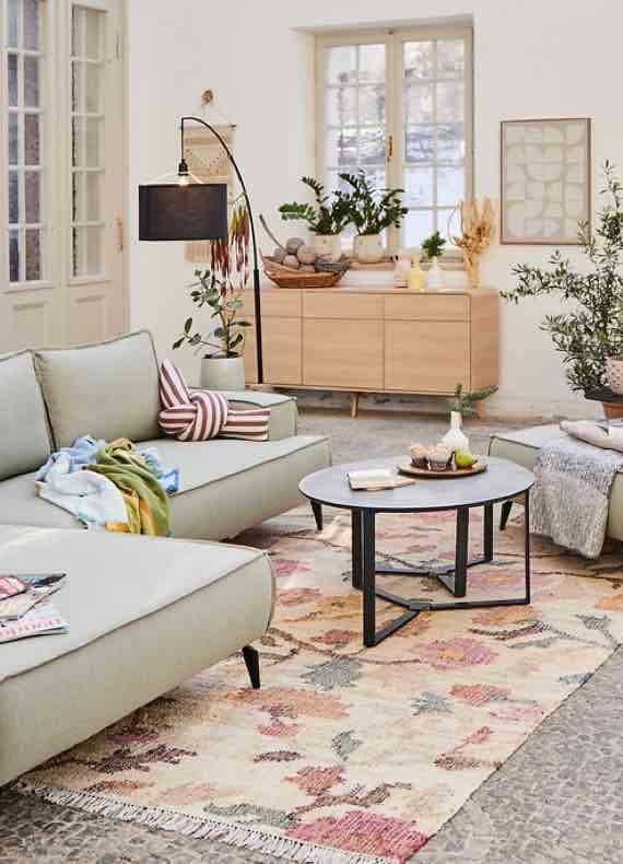 Helles Wohnzimmer mit Sofas, rundem Couchtisch und Sideboard, dekoriert mit Pflanzen und Teppich mit Blumenmuster
