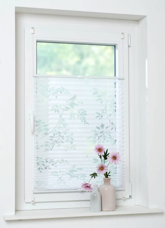 Weißes Fenster mit halb geschlossenem Faltrollo mit Blattmuster, auf der Fensterbank drei Vasen mit rosa Blumen