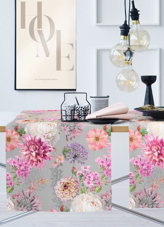 Tisch mit grauem Läufer mit bunten Blumen, darauf Geschirr und Deko, im Hintergrund Poster mit Schriftzug HOME