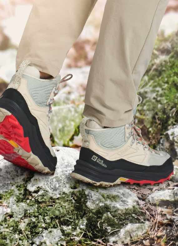 Person in beigefarbenen Wanderstiefeln auf steinigem, bemoostem Untergrund in der Natur