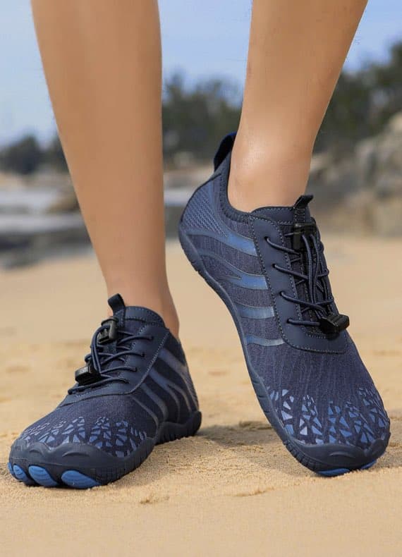Person am Strand trägt dunkelblaue Sportschuhe mit Zugband und Streifen, Nahaufnahme der Füße im Sand