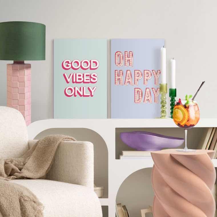 GOOD VIBES ONLY und OH HAPPY DAY – bunte Poster auf Sideboard mit Kerzen, Tischlampe, Sessel und Glas mit Obstdrink