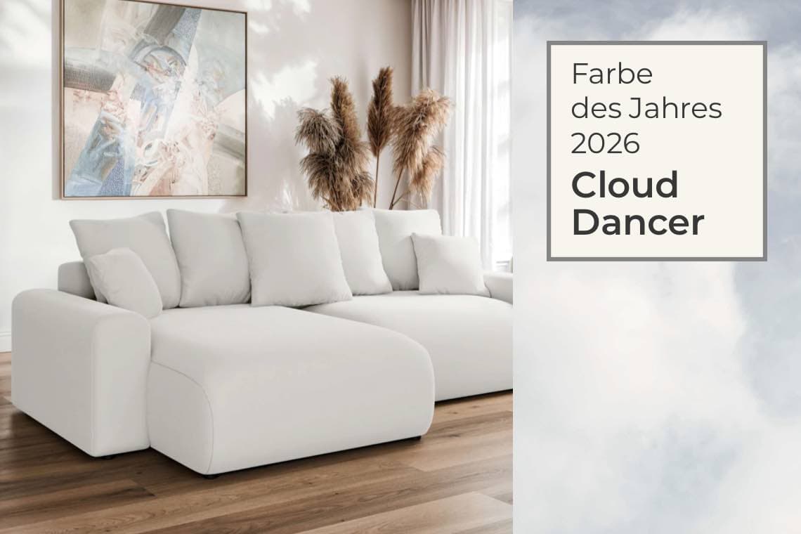 Farbe des Jahres 2026 Cloud Dancer – helles Sofa mit vielen Kissen vor Fenster, Bild und Gräsern im Wohnzimmer