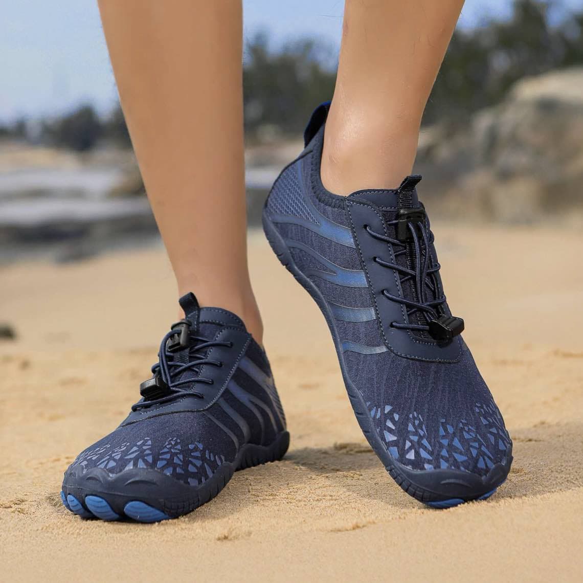 Person am Strand trägt dunkelblaue Sportschuhe mit Muster und elastischer Schnellschnürung