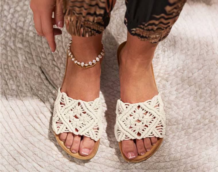 Füße in flachen Sandalen mit breiten geflochtenen Riemen, Fußkettchen mit Perlen, dazu gemusterte, hochgekrempelte Hose