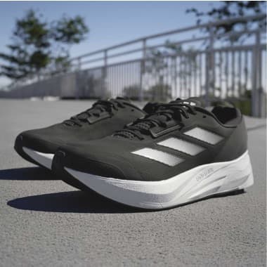 Schwarze Laufschuhe mit weißen Streifen und dicker weißer Sohle auf einem Weg im Freien vor einem Geländer