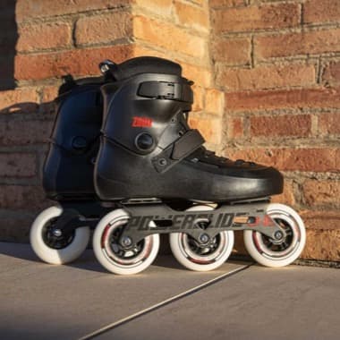 Schwarze Inline-Skates mit vier weißen Rollen stehen nebeneinander vor einer Ziegelwand auf dem Boden