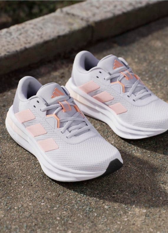 Sportliche Sneaker in Hellgrau mit rosa Details stehen nebeneinander auf einem Gehweg draußen