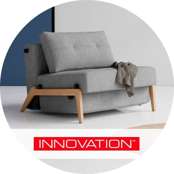 INNOVATION – graues Schlafsofa mit Holzfüßen, Rückenlehne halb hochgestellt, Decke über der Sitzfläche