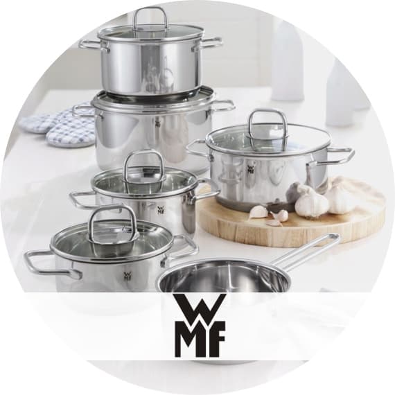 WMF Logo vor Set aus glänzenden Kochtöpfen mit Deckel, daneben Schneidebrett mit Knoblauch in heller Küche