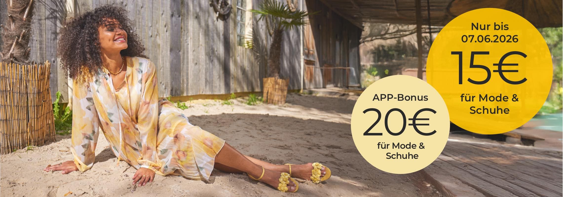 15€ für Mode & Schuhe, 20€ APP-Bonus – Frau im gemusterten Kleid sitzt im Sand vor Holzhütte