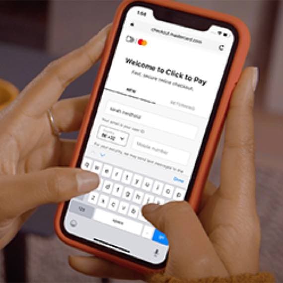 Welcome to Click to Pay – Person hält Smartphone in roter Hülle und tippt Zahlungsdaten in ein Online-Formular