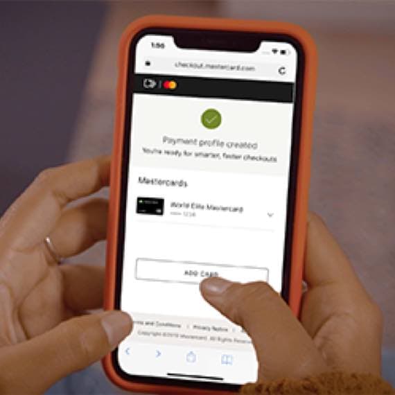 Payment profile created – Person hält Smartphone mit geöffneter Mastercard-Checkout-Seite in beiden Händen