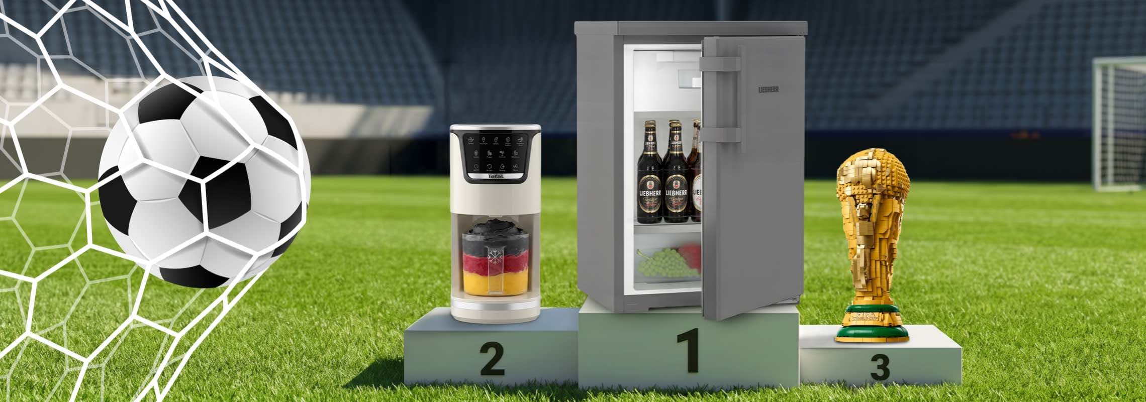 Fußball im Netz, daneben auf Siegerpodest Minikühlschrank, Getränkespender und goldener Pokal im Stadion