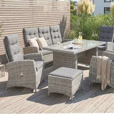 Garten-Sitzgruppe mit grauen Polstern auf Holzterrasse, Tisch mit Karaffe und Gläsern, Decke über Stuhllehne
