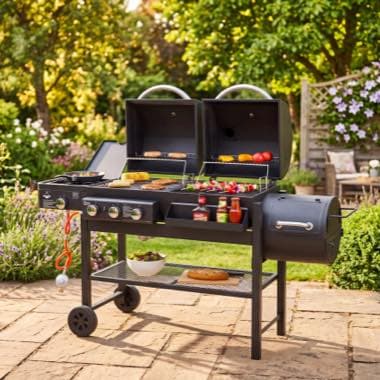 Großer Grillwagen im Garten, mit geöffneten Deckeln, Würstchen, Spießen und Gemüse auf dem Rost