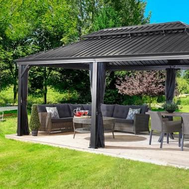 Gartenpavillon auf Holzterrasse mit Ecksofa, Tisch mit Getränken und Essgruppe, umgeben von Rasen und Bäumen