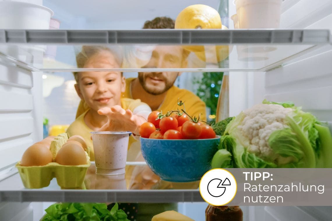 TIPP: Ratenzahlung nutzen – Vater und Kind greifen durch offene Kühlschranktür nach einer Schale mit Tomaten