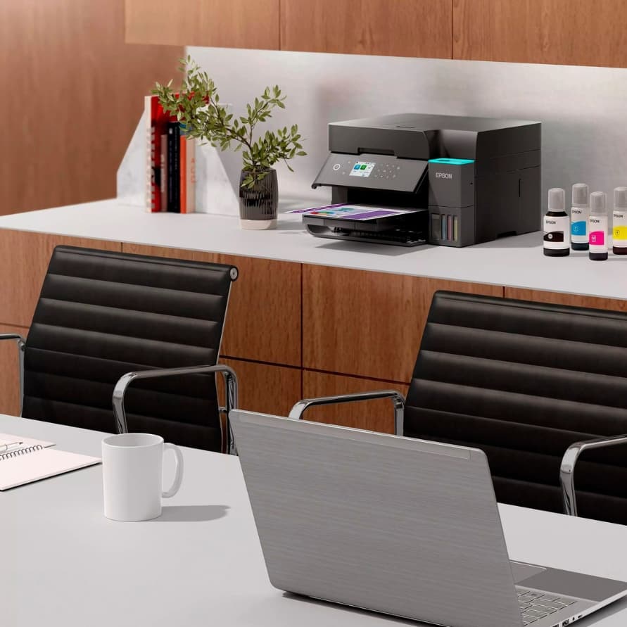 Moderner Konferenzraum mit zwei Stühlen, Laptop auf Tisch und Epson-Drucker mit Tintenflaschen auf Sideboard