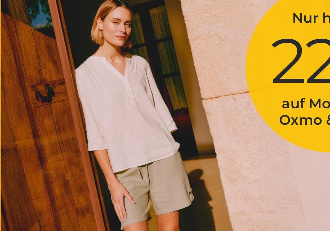 Nur heute 22 % auf Mode von Oxmo – Frau in heller Bluse und Shorts steht in einer offenen Holztür