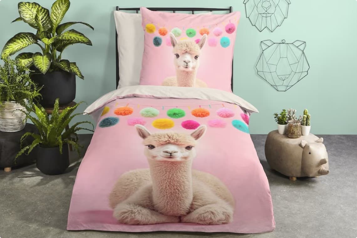 Rosa Kinderbettwäsche mit großem Lama-Motiv und bunten Pompons, dekoriert mit Pflanzen und Tierfiguren im Zimmer