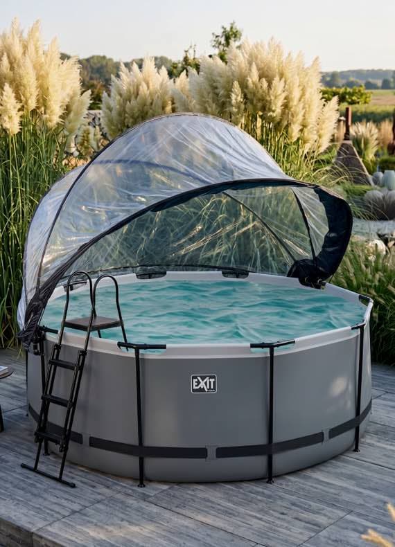 Runder Aufstellpool mit Leiter und geöffneter transparenter Abdeckung auf Terrasse, umgeben von hohen Ziergräsern